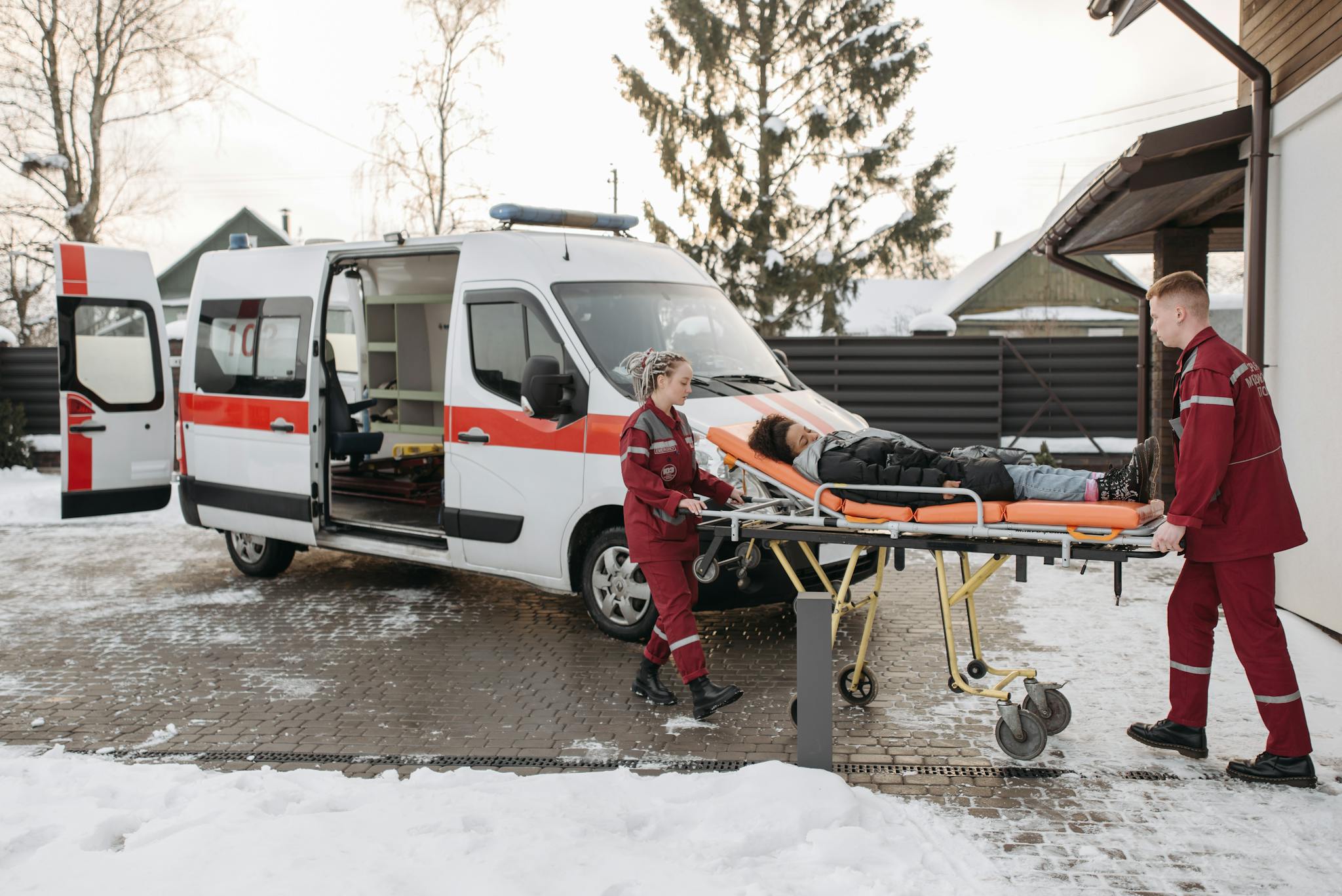 Paramedics transporting a patient on a stretcher to an ambulance on a snowy day.