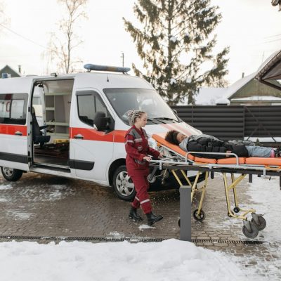 Paramedics transporting a patient on a stretcher to an ambulance on a snowy day.